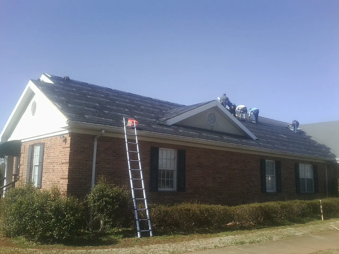 Crew tearing shingles off a brick ranch roof with a ladder set — Metal Roof Repair work by our crew in Bartlett