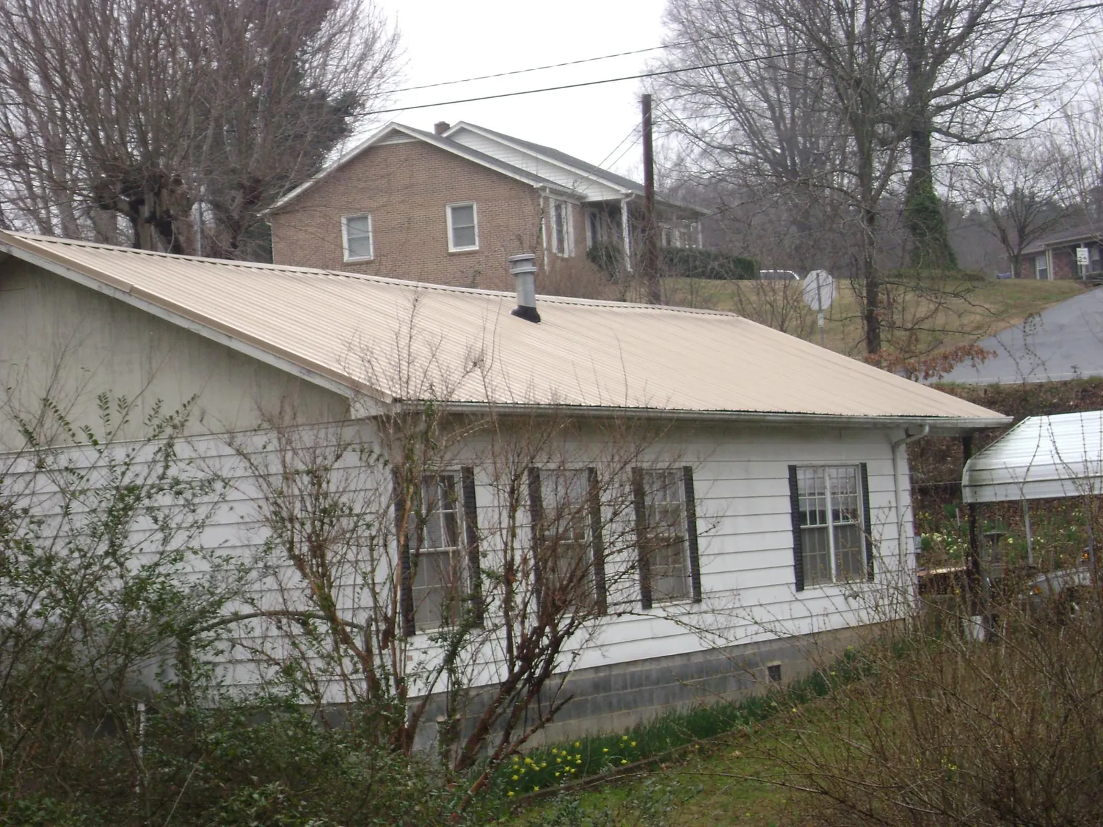 Tan metal roof on a white sided house set into a hillside — Commercial Roofing by Roofing Brothers in Bartlett